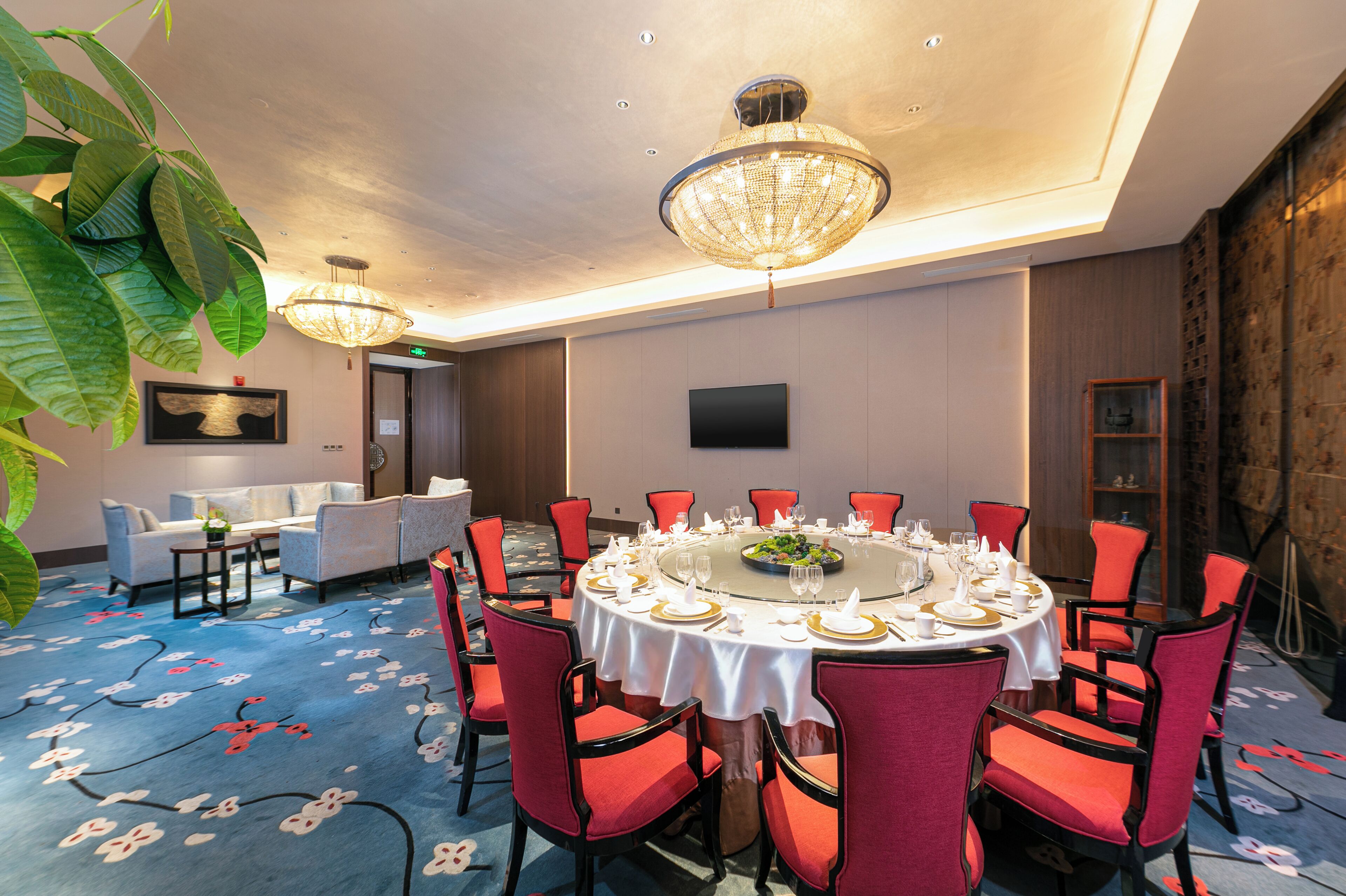 A conference room with a round table, red chairs, and a chandelier.