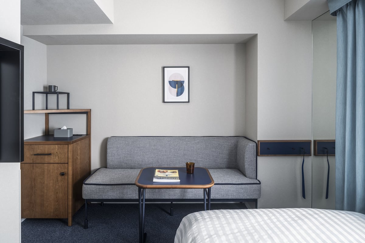 Une chambre d’hôtel équipée d’un lit, d’un canapé, d’une petite table, d’un bureau et d’un téléviseur fixé au mur.