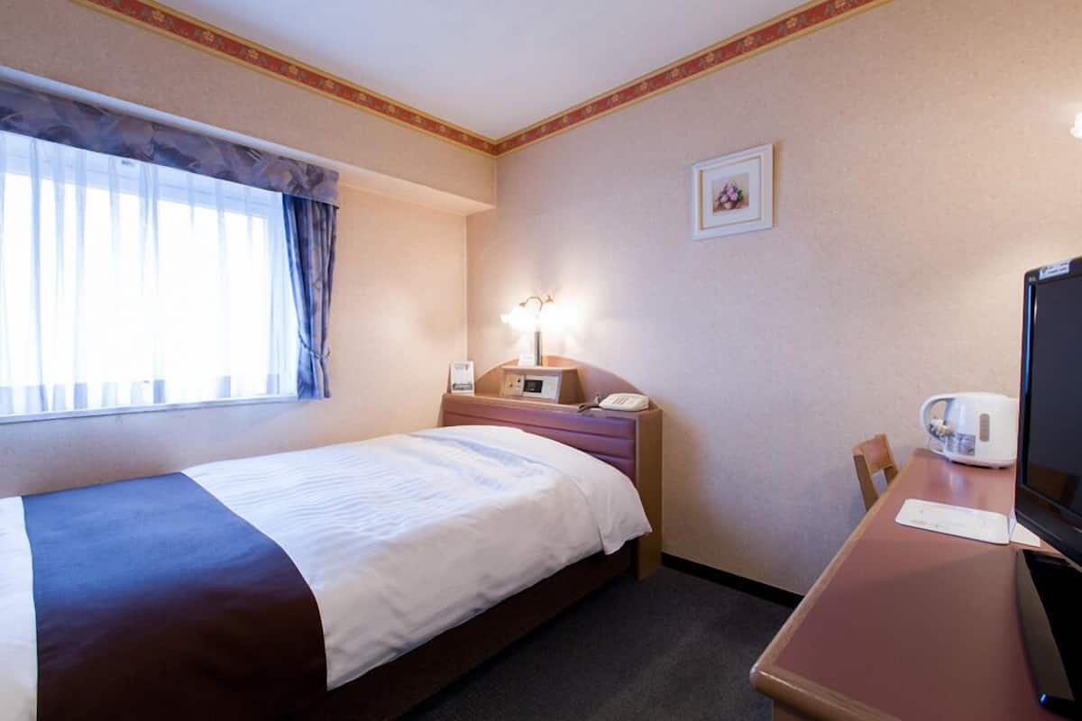 Une chambre d’hôtel avec un lit, un bureau avec un ordinateur, un téléphone, une lampe et un tableau au mur.