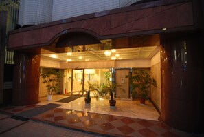 Entrada de hotel con suelo a cuadros, plantas en macetas y puerta de vidrio que da al interior.