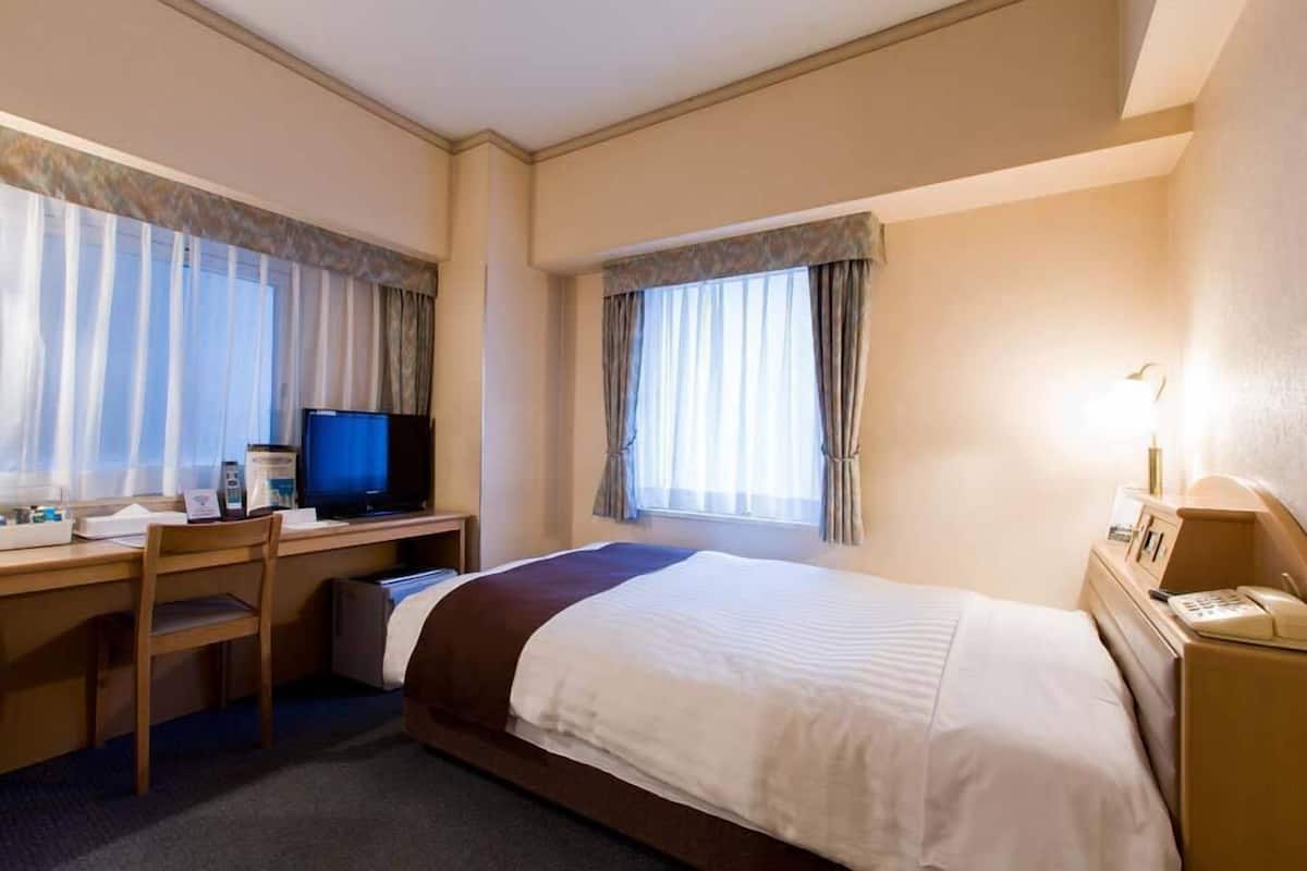 Une chambre d’hôtel équipée d’un lit, d’un bureau, d’une chaise, d’une télévision et d’un téléphone sur la table de chevet.