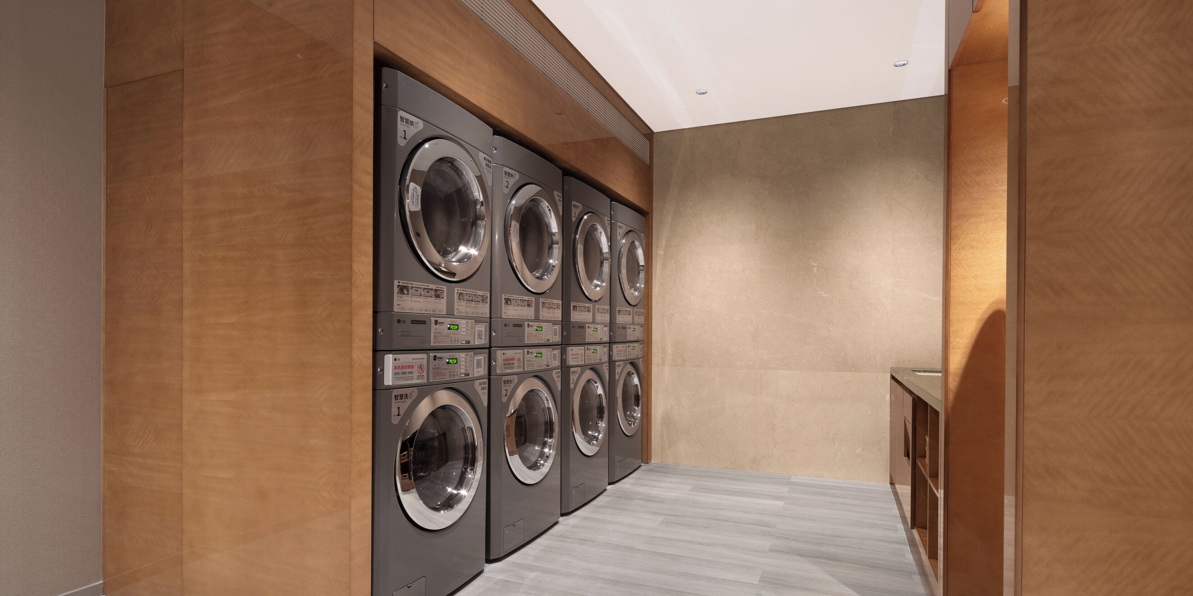 A laundry room with multiple washing machines and dryers, wooden walls, and a tiled floor.