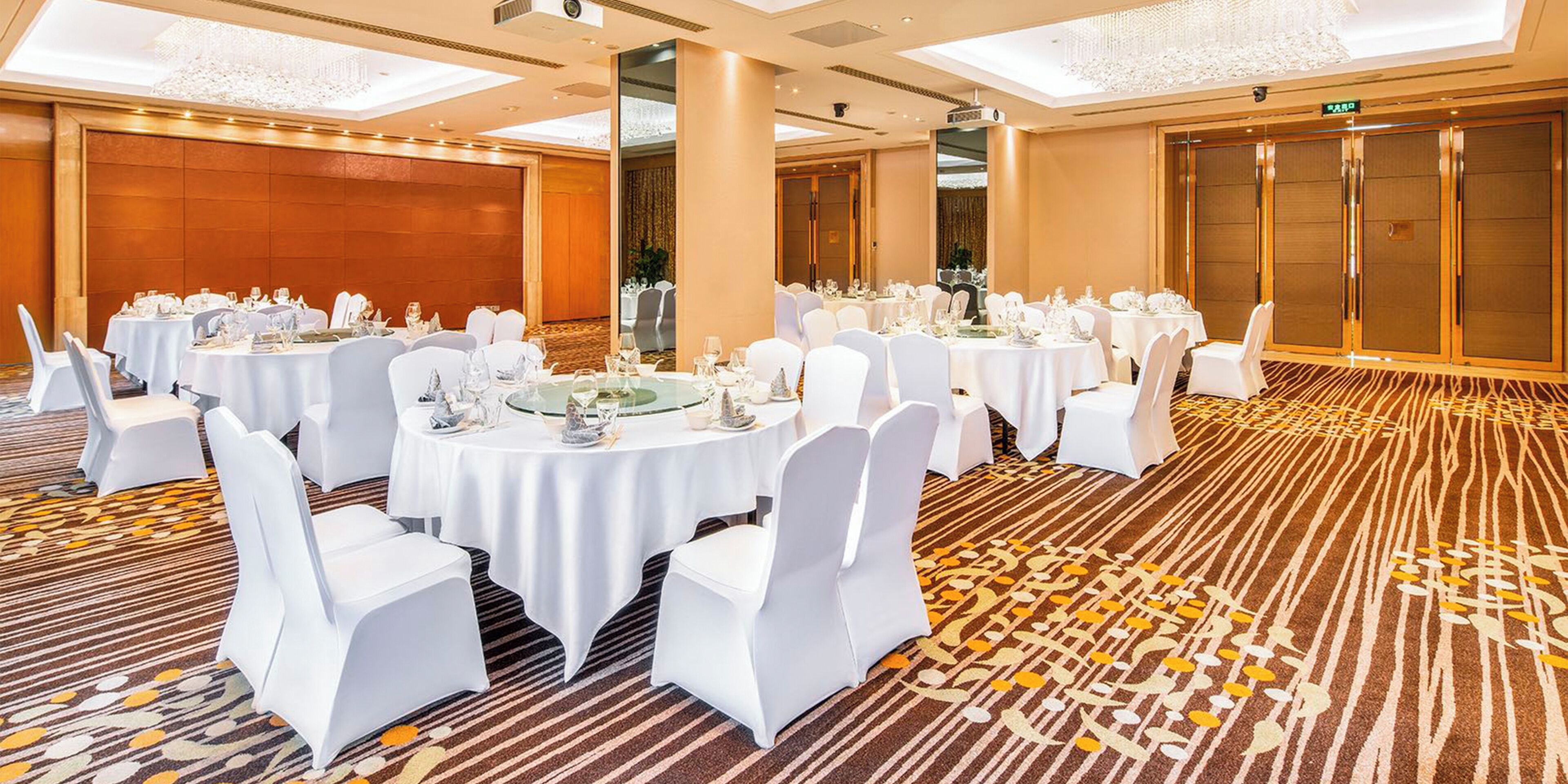 A banquet hall with round tables set for dining, white chairs, and a carpeted floor.