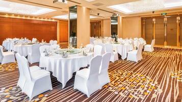 Un salón de banquetes con mesas redondas dispuestas para comer, sillas blancas y suelo alfombrado.