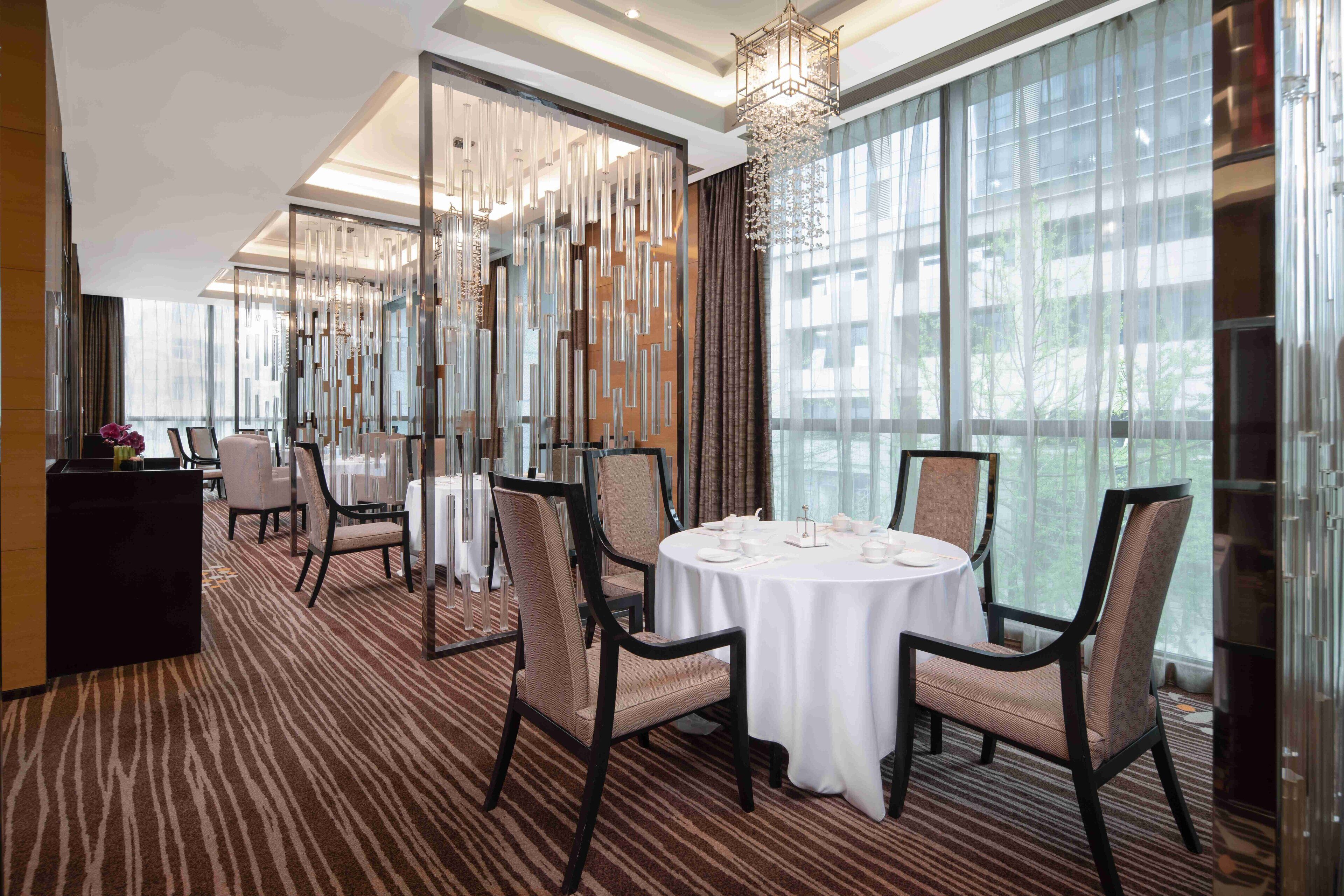 A modern dining area with a round table set for four, surrounded by chairs, in a room with large windows and a patterned carpet.