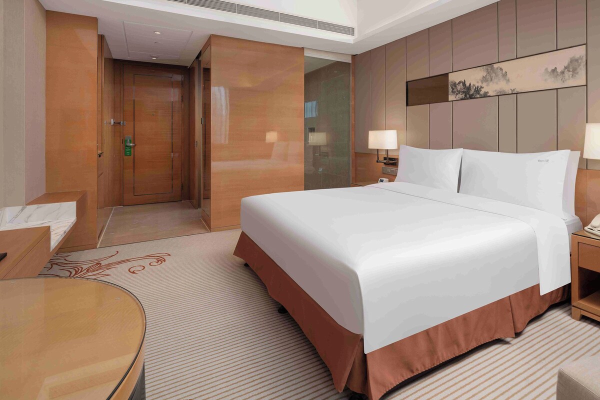 A hotel room with a large bed, bedside tables, a desk, and a chair.