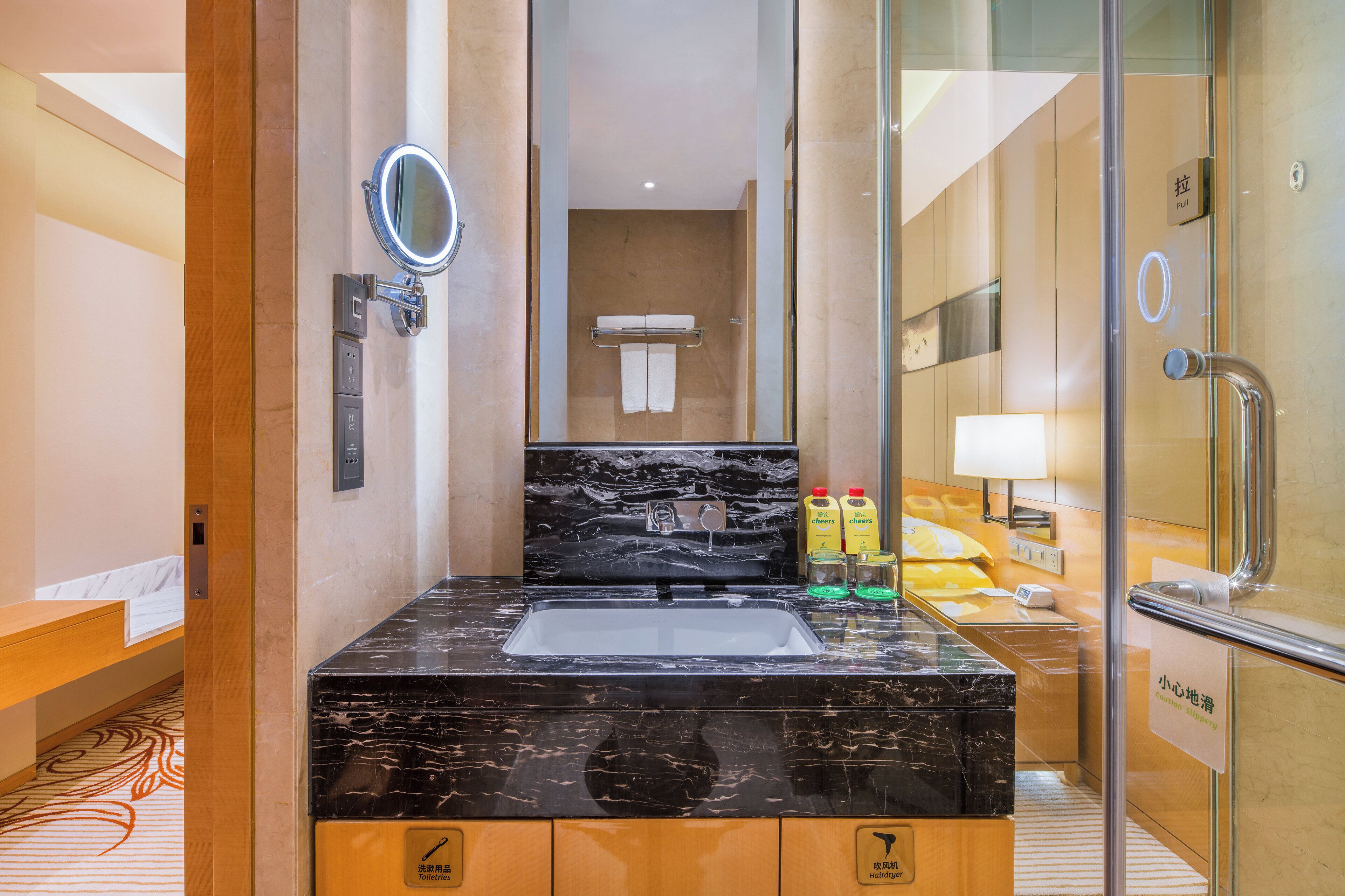 Un bagno d'hotel con lavabo in marmo nero, uno specchio, un portasciugamani e un box doccia in vetro.