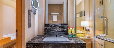 Un bagno d'hotel con lavabo in marmo nero, uno specchio, un portasciugamani e un box doccia in vetro.