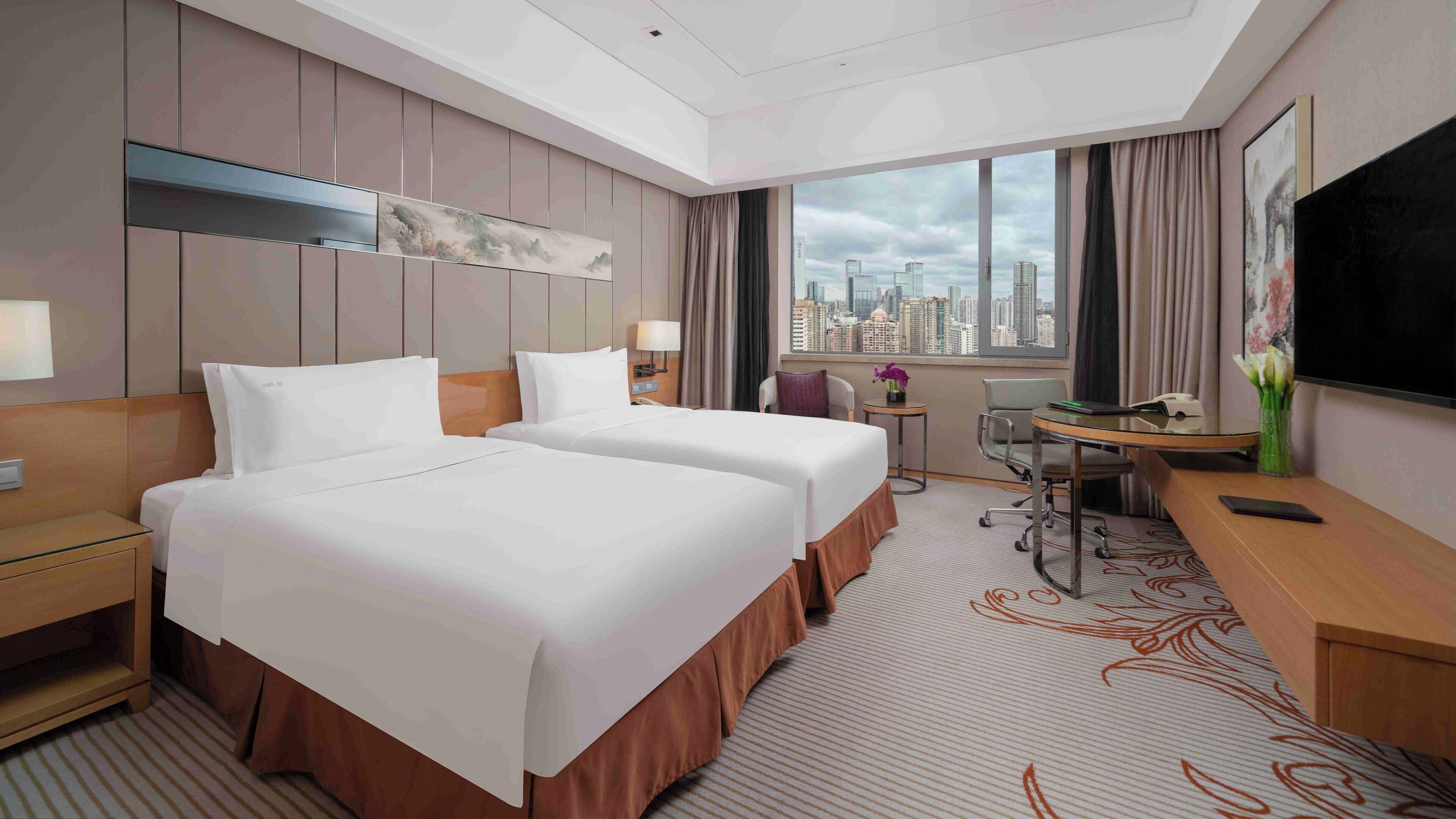 A hotel room with two beds, a desk, a chair, a TV, and a city view.
