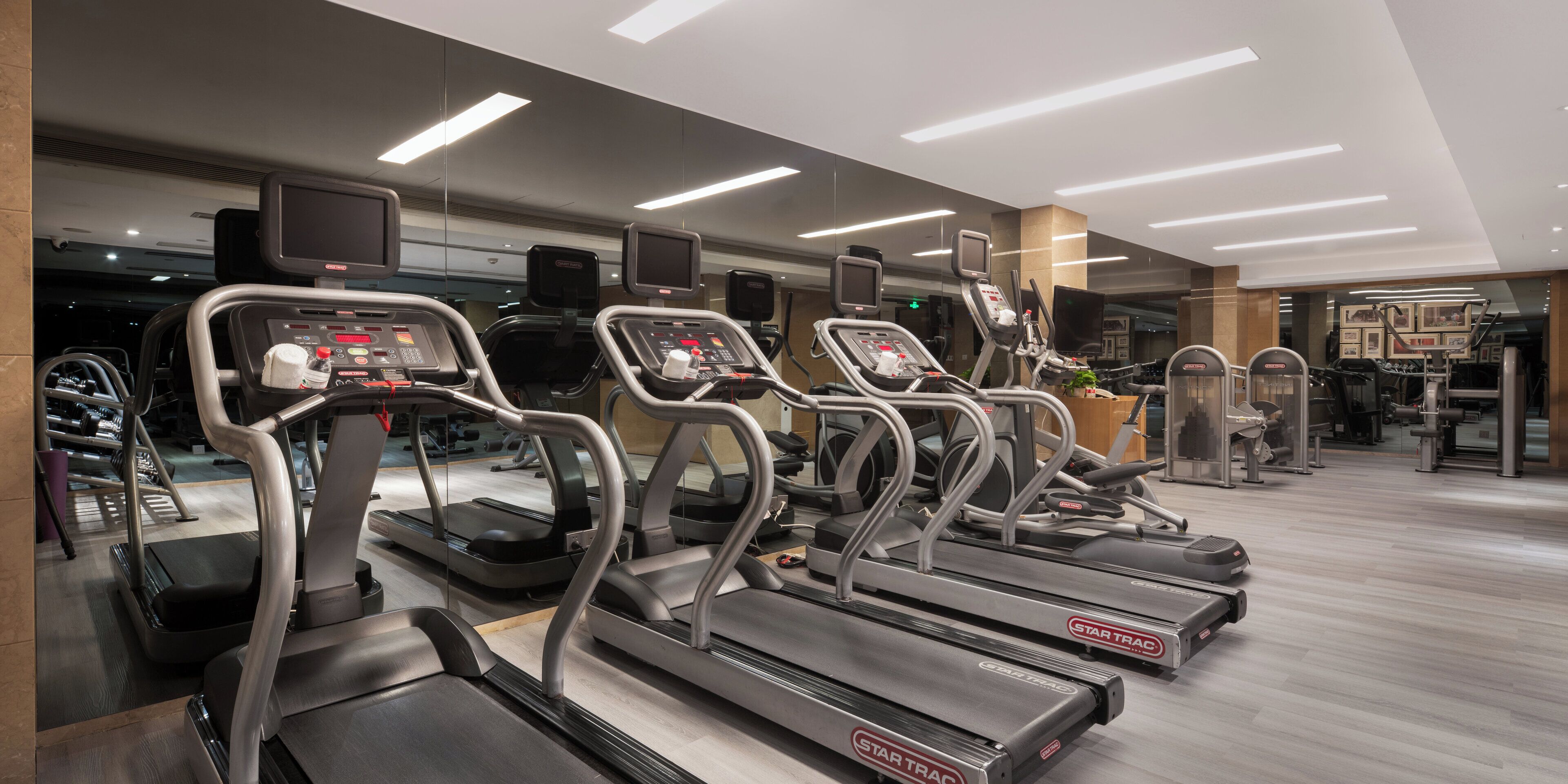 Ein Fitnessraum mit mehreren Laufbändern, Ergometer und einer Spiegelwand.