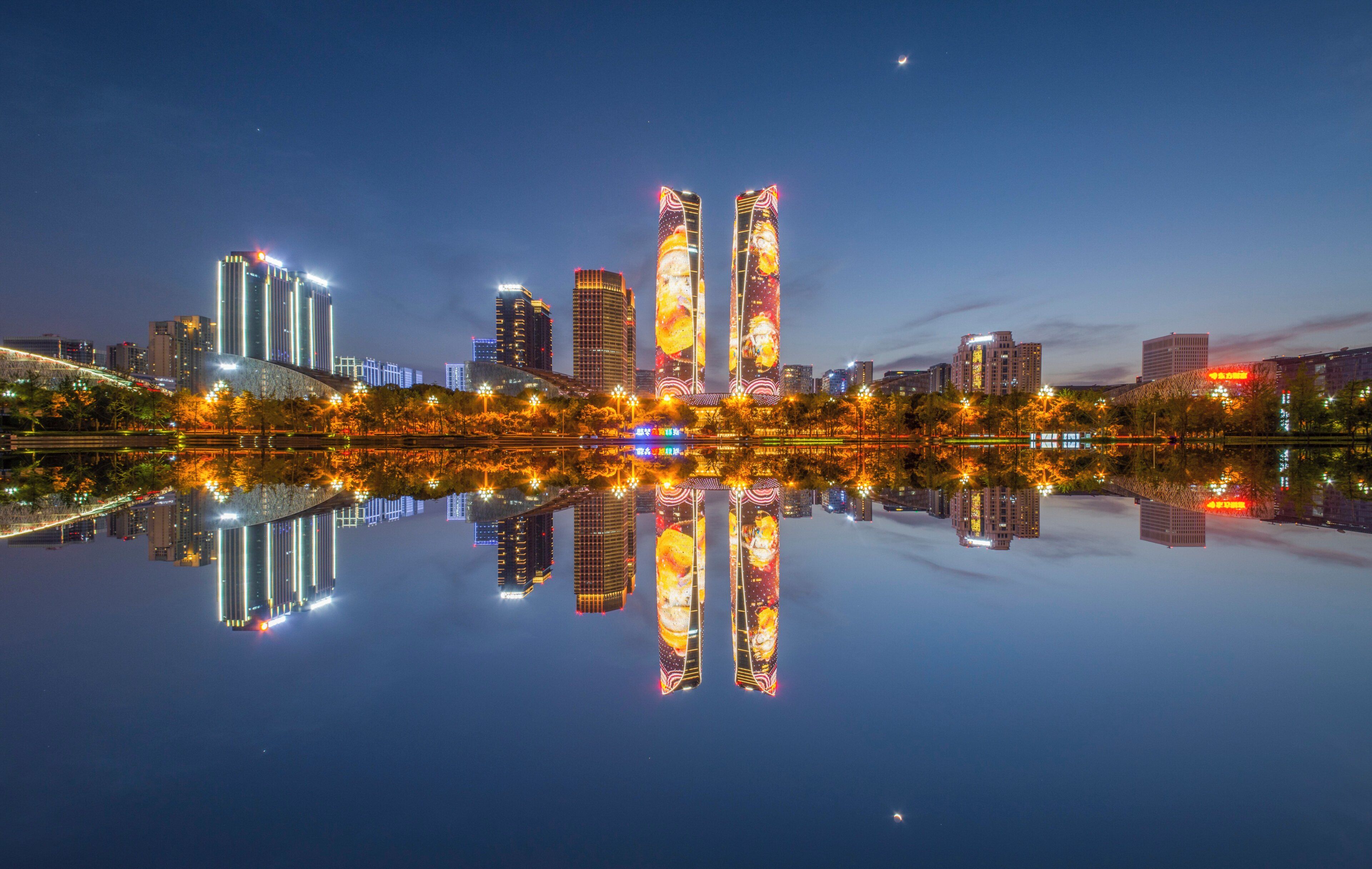 Un paisaje urbano nocturno con edificios iluminados que se reflejan en aguas tranquilas.
