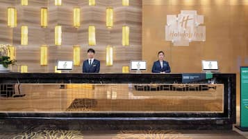 A hotel reception desk with two staff members, a sign for the Holiday Inn, and a sign for the IHG Rewards Club.