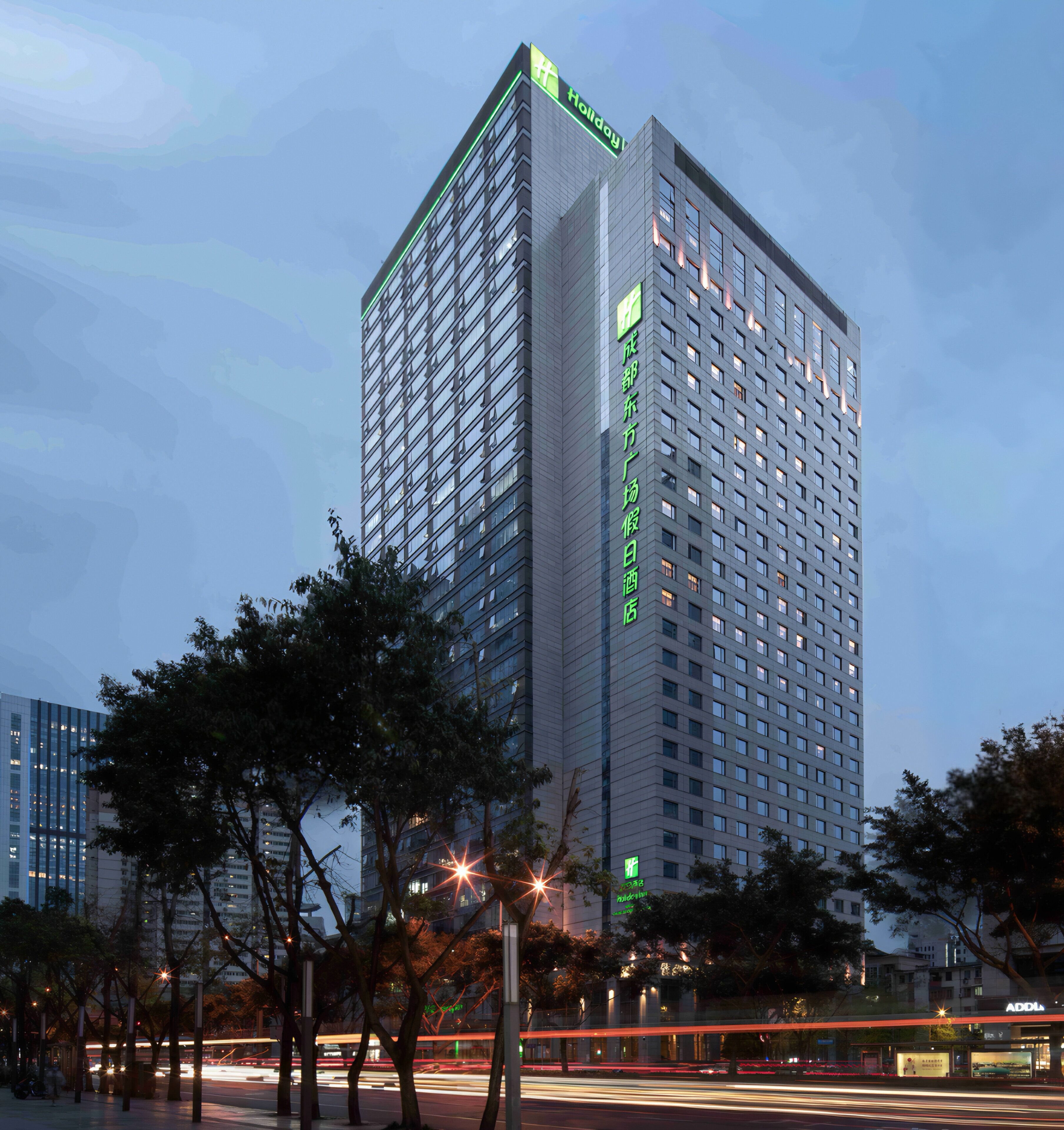 A high-rise hotel with a modern design, featuring a prominent green sign at the top.