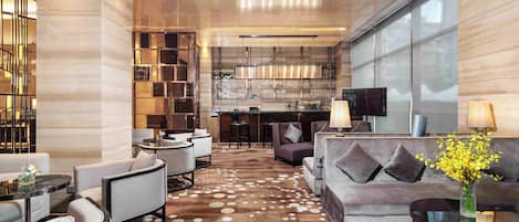 Un moderno vestíbulo de hotel con una zona de bar, disposición de asientos y un amplio ventanal que proporciona luz natural.