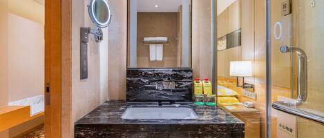 A modern bathroom with a black marble sink, a glass shower enclosure, and a mirror with a round frame.