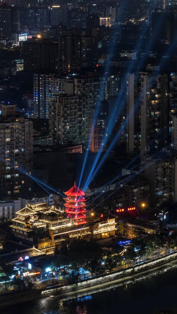 A cityscape at night with a prominent pagoda illuminated by beams of light.