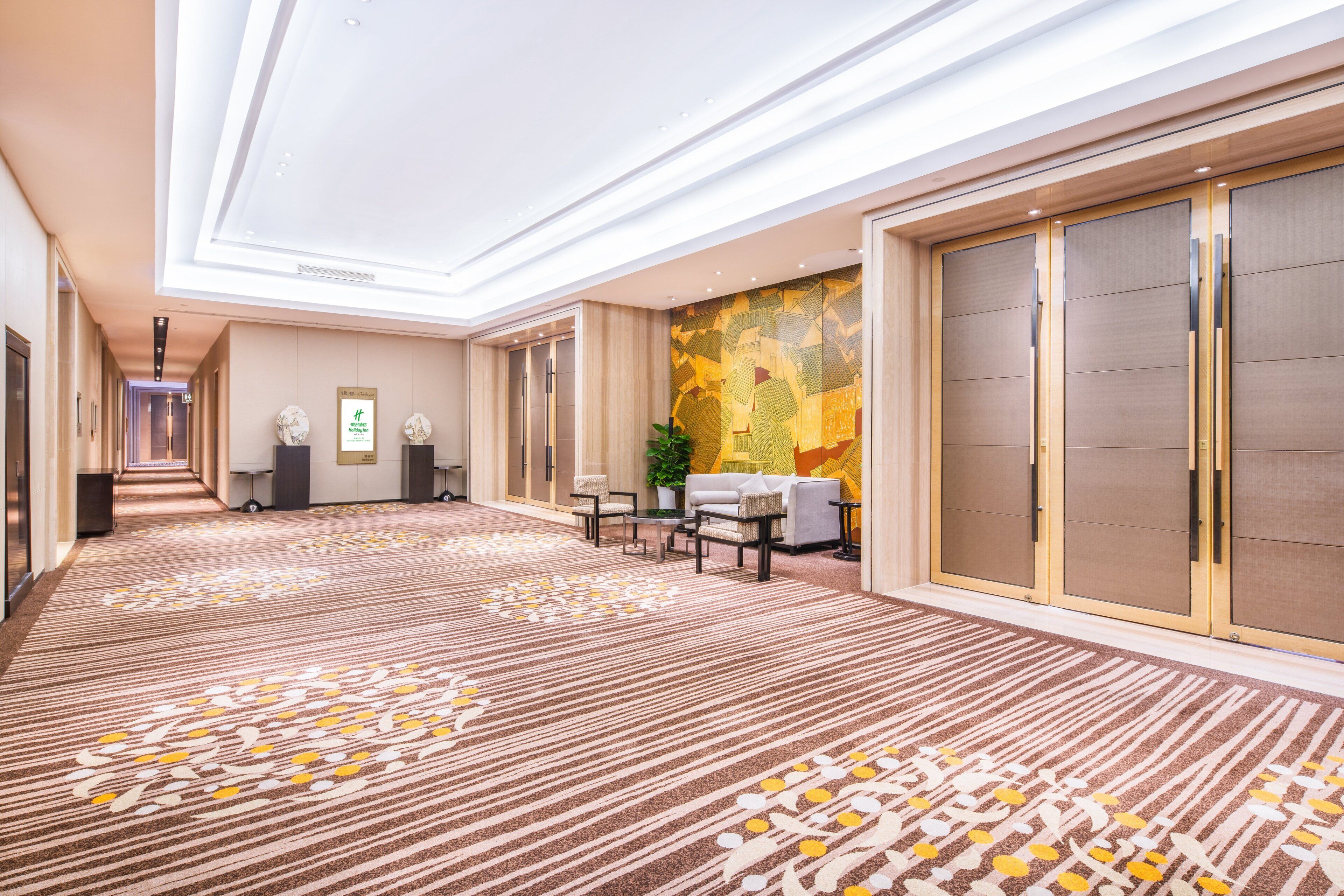 A hotel corridor with a patterned carpet, a reception desk, seating area, and a large sliding door.
