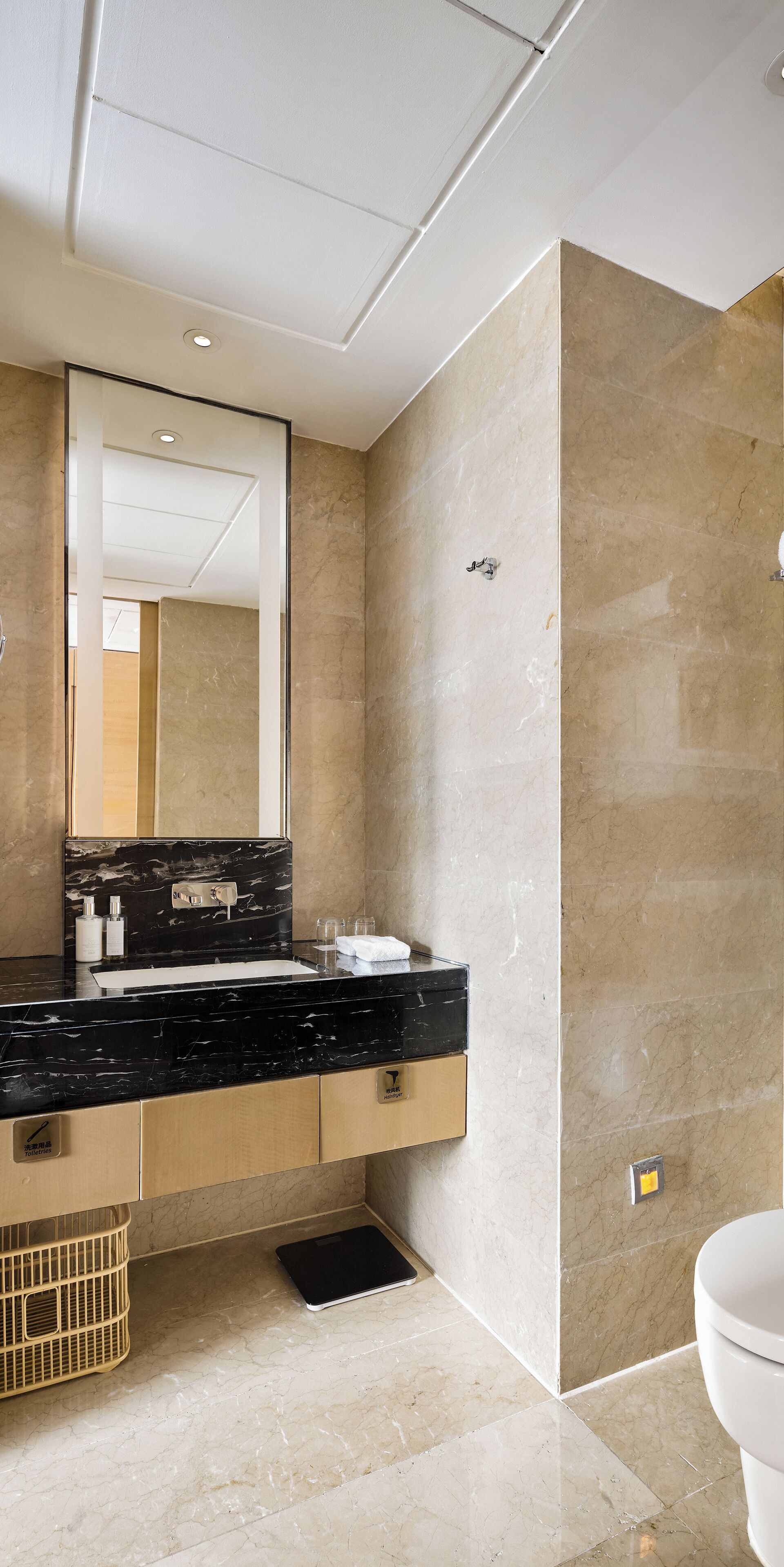 A modern bathroom with a black marble sink, a large mirror, and beige marble walls.