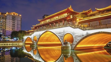 Un puente chino tradicional con barandillas doradas ornamentales y su reflejo en el agua.