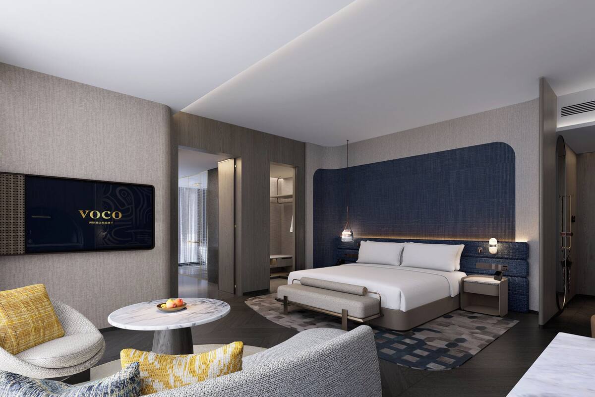 Ein modernes Hotelzimmer mit einem großen Bett, einer Sitzecke mit rundem Tisch und einem an der Wand montierten Fernseher.