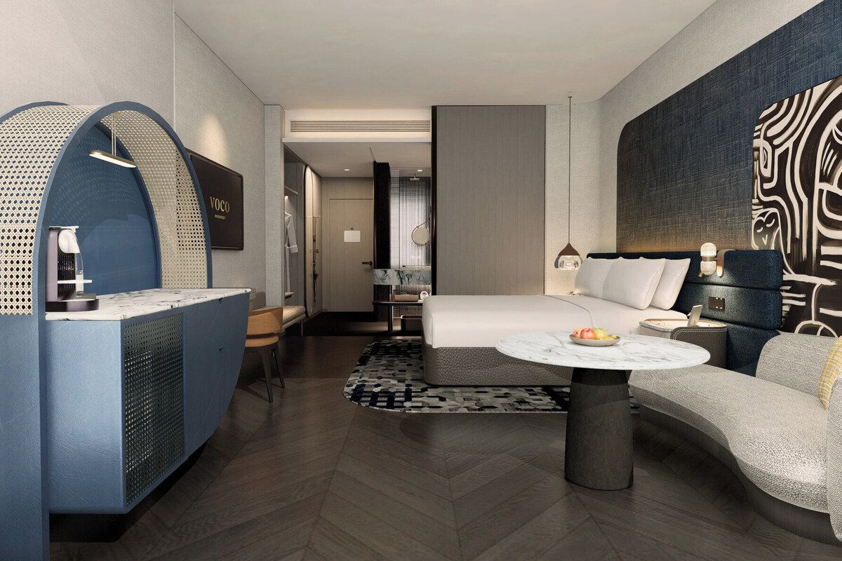 Een moderne hotelkamer met een bed, een bank, een bijzettafeltje, een bureau en een groot abstract schilderij aan de muur.