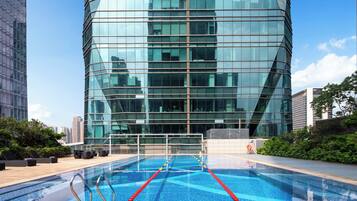 Un bâtiment moderne doté d’une façade en verre réfléchissant, d’une piscine sur le toit avec des lignes de démarcation pour les couloirs de nage, et entouré de verdure.