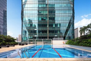 A modern building with a reflective glass facade, a rooftop pool with lane markers, and surrounding greenery. - voco Suites Shenzhen Huanggang by IHG (Shenzhen)