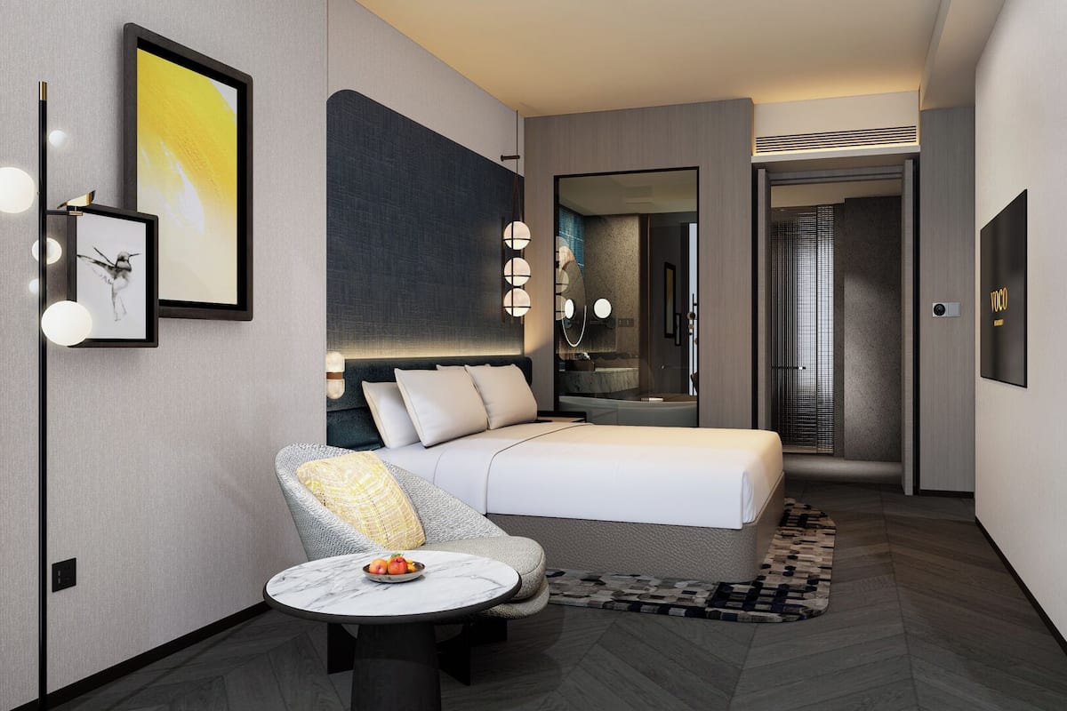 Ein modernes Hotelzimmer mit Bett, einer Sitzecke mit Tisch, einem großen Spiegel und Blick ins Badezimmer.