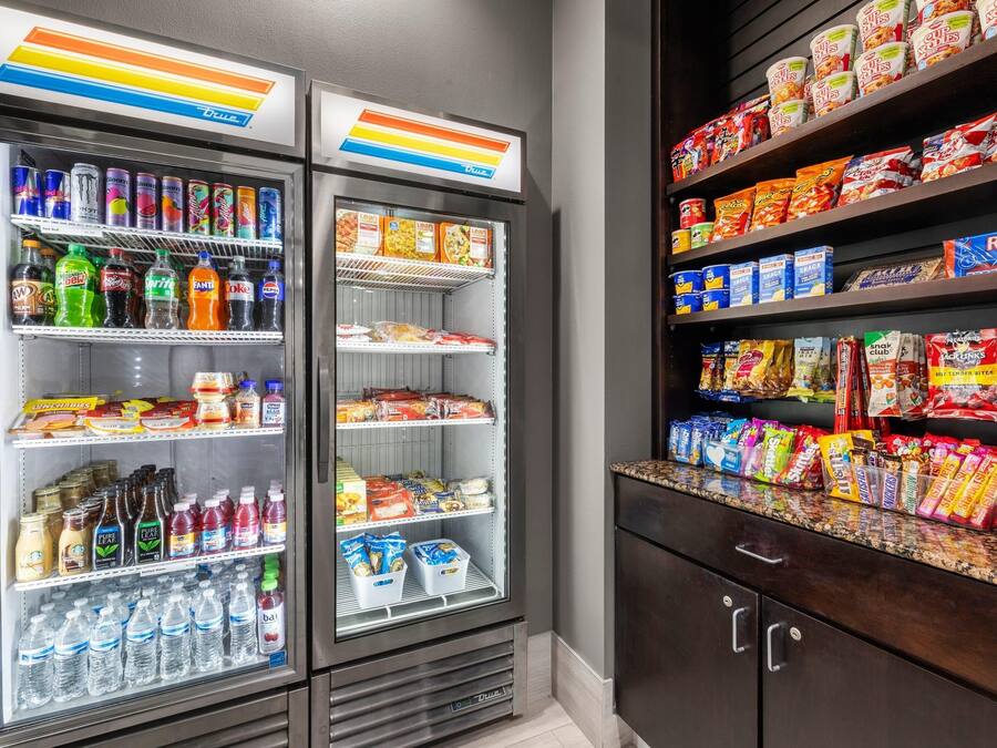 Una máquina expendedora llena de bebidas y aperitivos, un estante con productos envasados y un mostrador con más opciones de bocadillos.