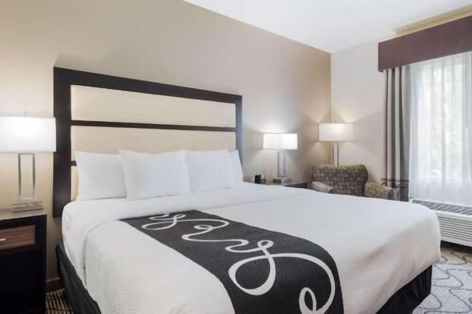 A hotel room with a bed, two bedside lamps, a chair, and a window with curtains.