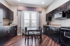 Una cocina moderna con armarios oscuros, una mesa de comedor con sillas, una ventana con cortinas y electrodomésticos integrados.