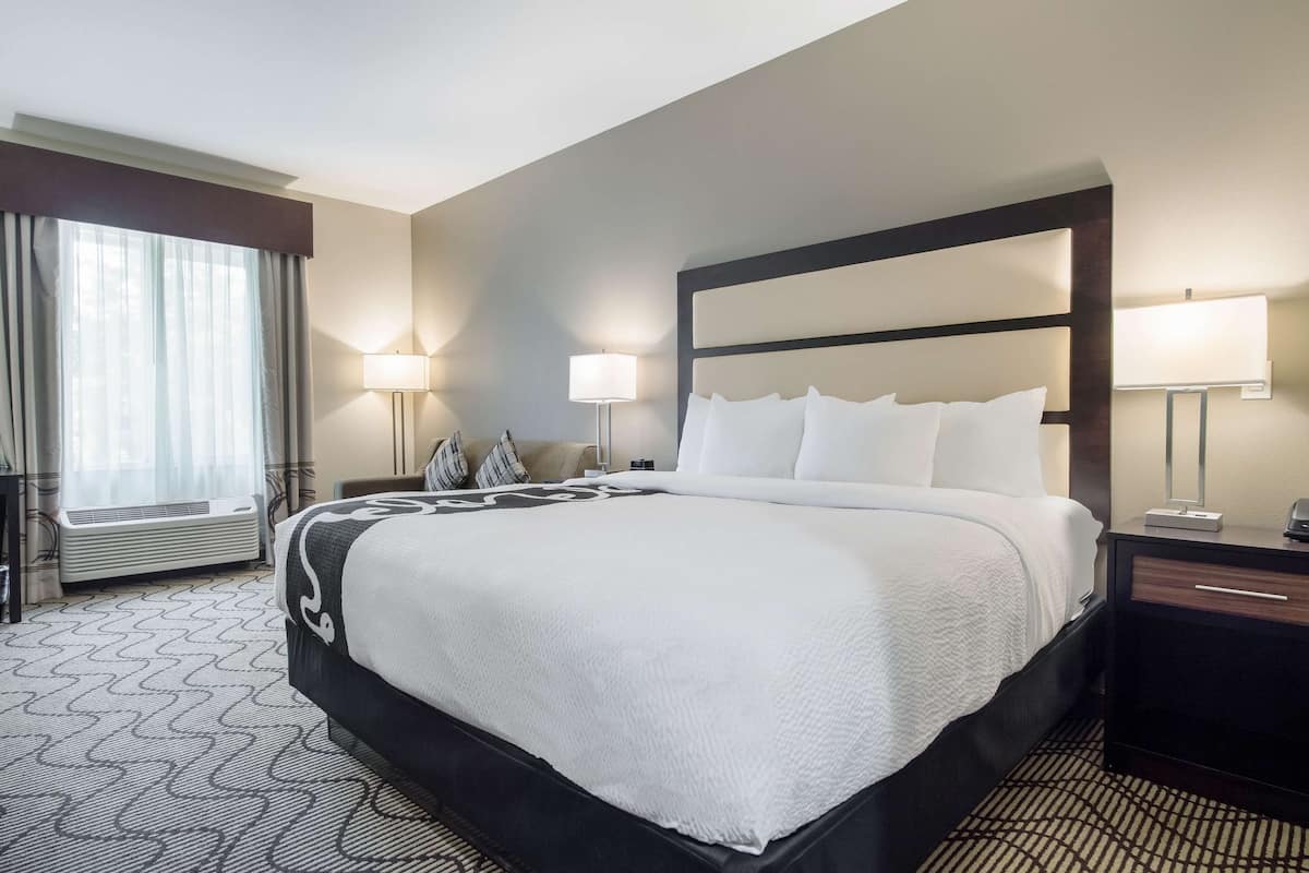 Ein Hotelzimmer mit einem großen Bett, Nachttischlampen, einem Schreibtisch und einem Fenster mit Vorhängen.