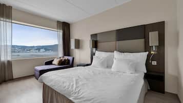 Habitación de hotel con una cama grande, vistas a la ciudad, un sofá y una mesita de noche con una lámpara.