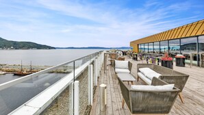 Une terrasse avec des sièges extérieurs, offrant une vue sur une étendue d’eau et sur une côte lointaine.