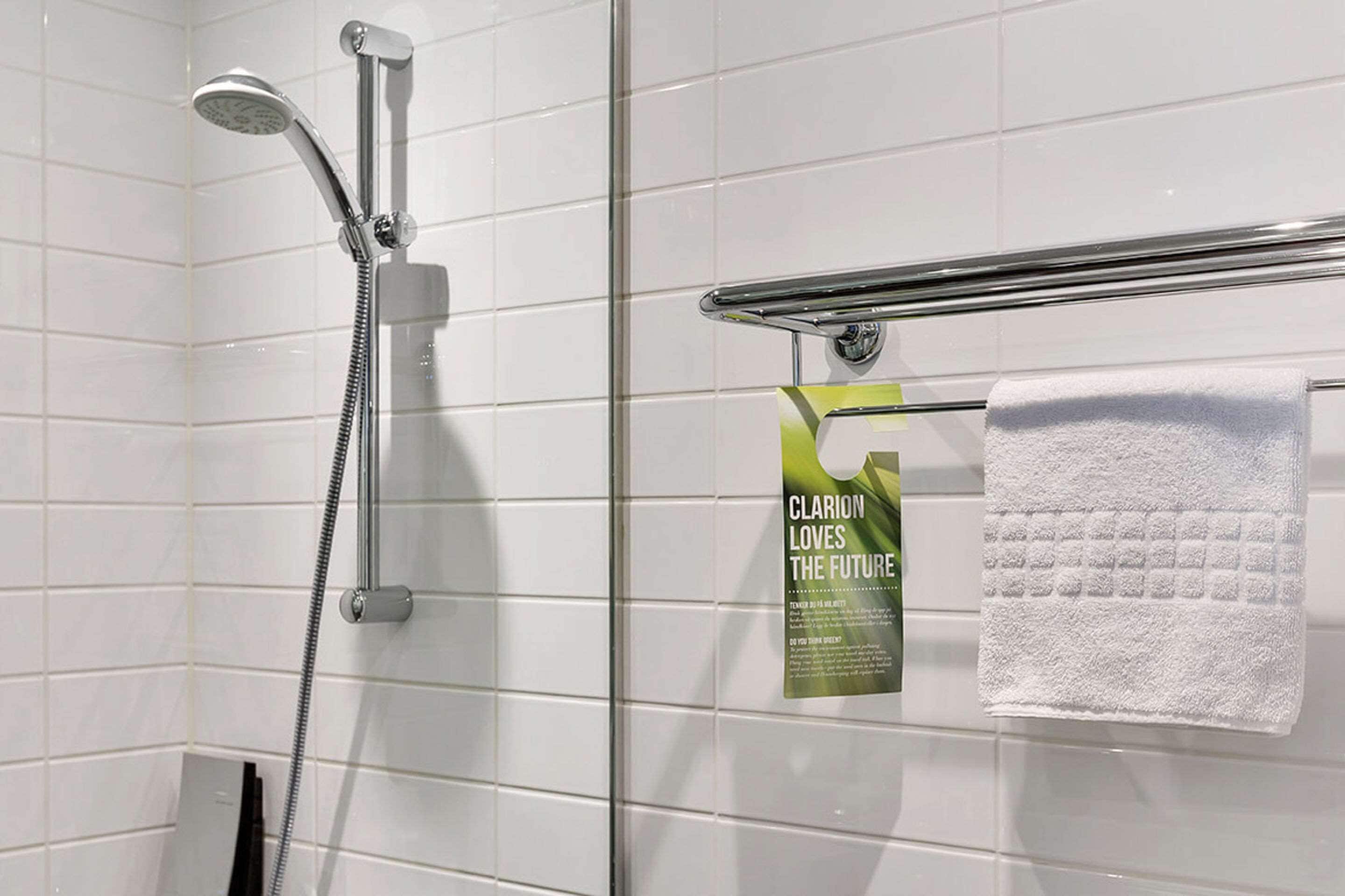 A shower with a handheld showerhead and a towel rack with a white towel. A poster is attached to the wall.