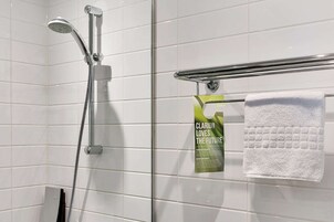 A shower with a handheld showerhead and a towel rack with a white towel. A poster is attached to the wall.
