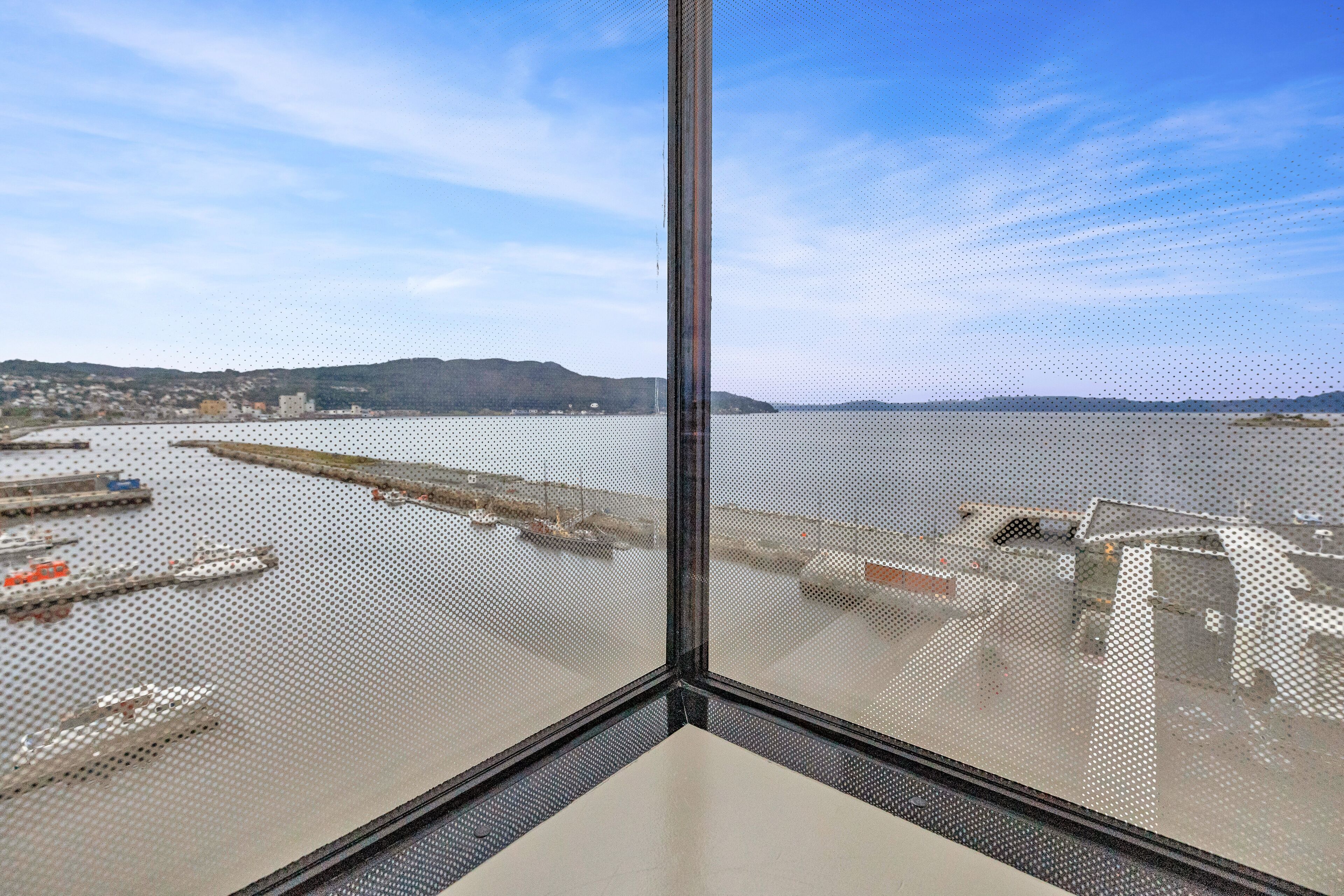 A view from a high-rise window overlooking a harbor with ships and industrial buildings.