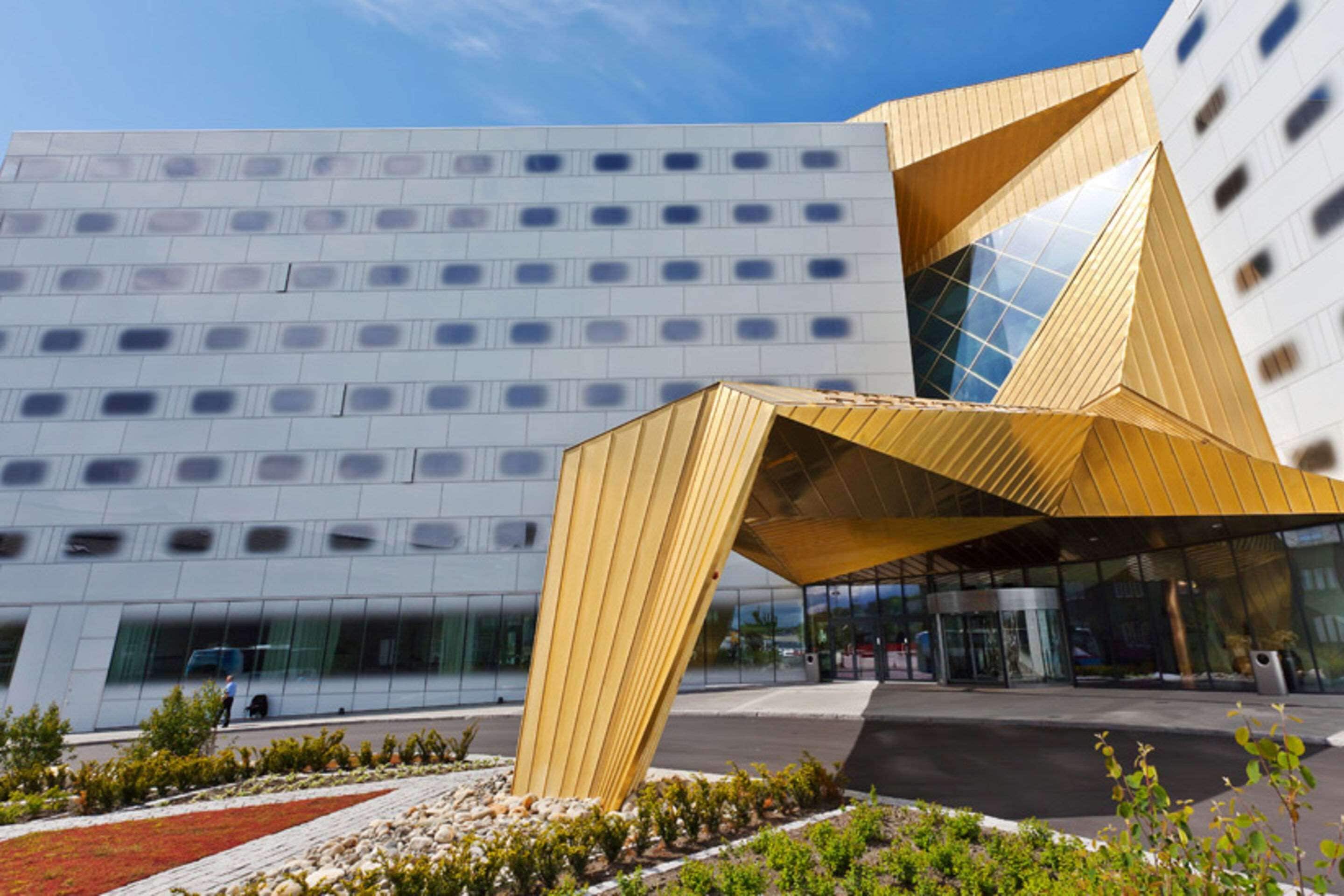 Un edificio moderno con un llamativo dosel geométrico en la entrada y fachada de vidrio reflectante.