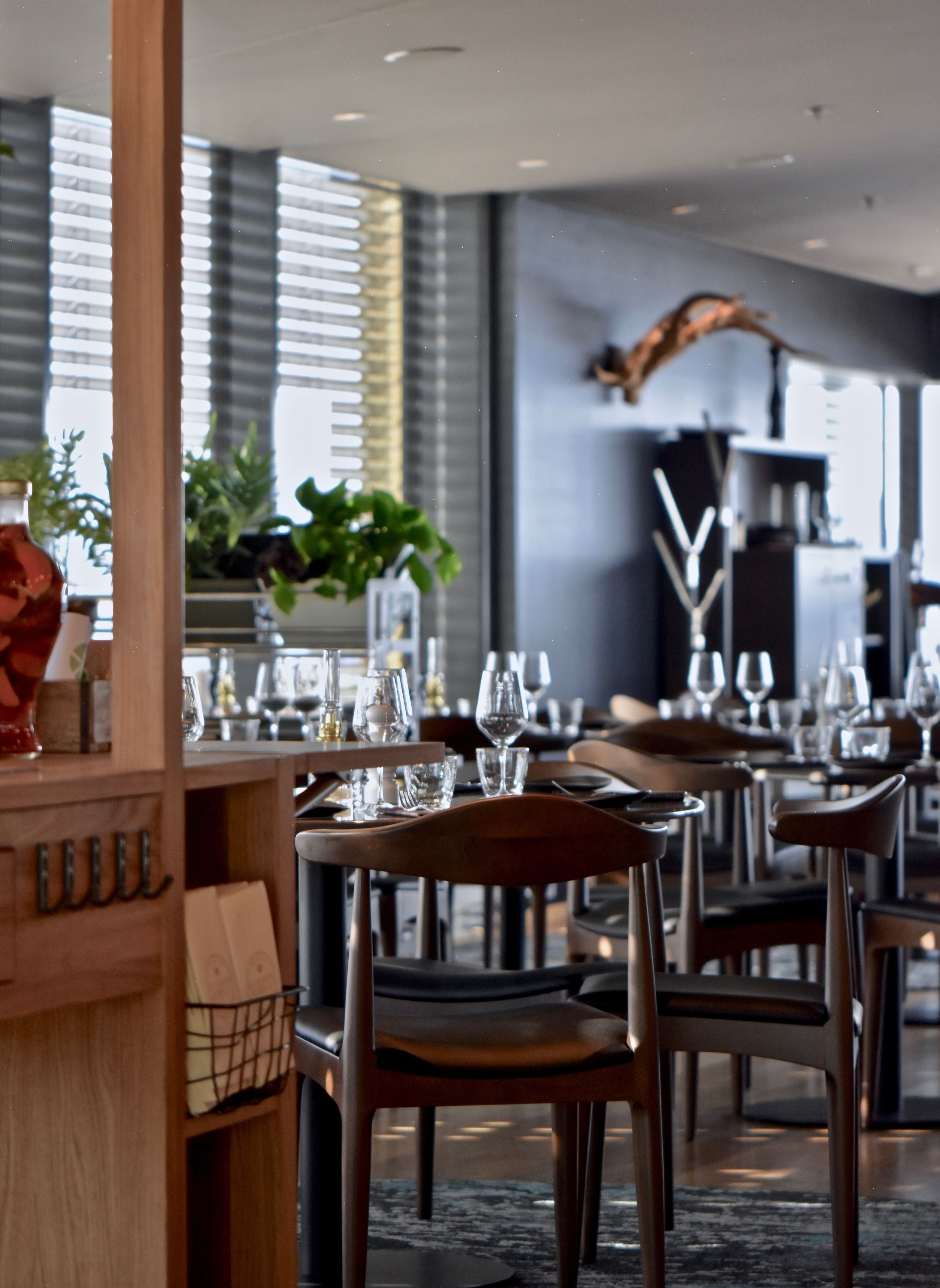 Interior moderno de restaurante con mesas y sillas de madera, cristalería y una escultura decorativa de un pájaro.