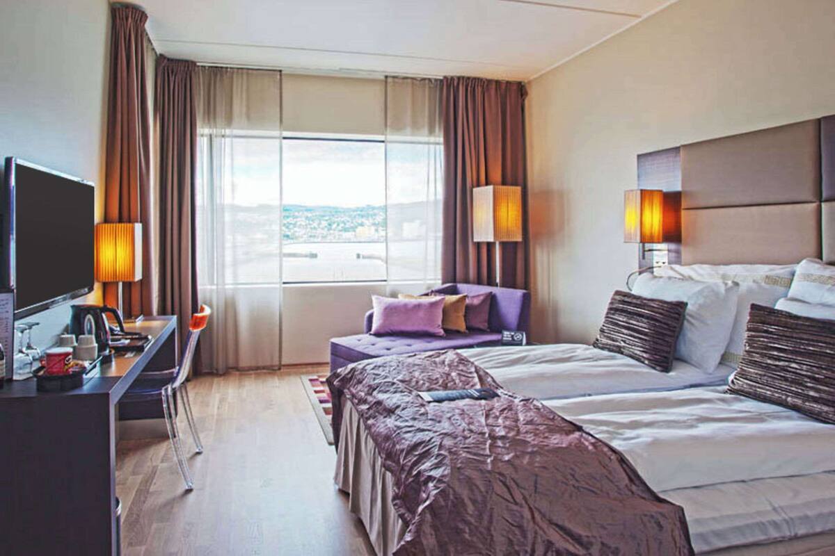 A hotel room with a bed, a desk, a television, and a window with curtains.