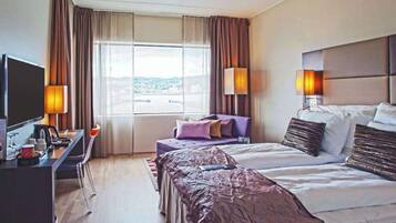 A hotel room with a bed, a desk, a television, and a window with curtains.