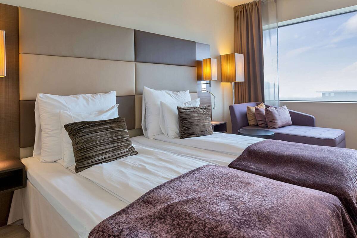 A hotel room with a large bed, two bedside tables, a chair, and a window with a view.