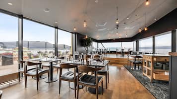 Un vaste espace dédié à la salle à manger, doté de grandes fenêtres, de tables et de chaises en bois, et offrant une vue sur le paysage urbain.
