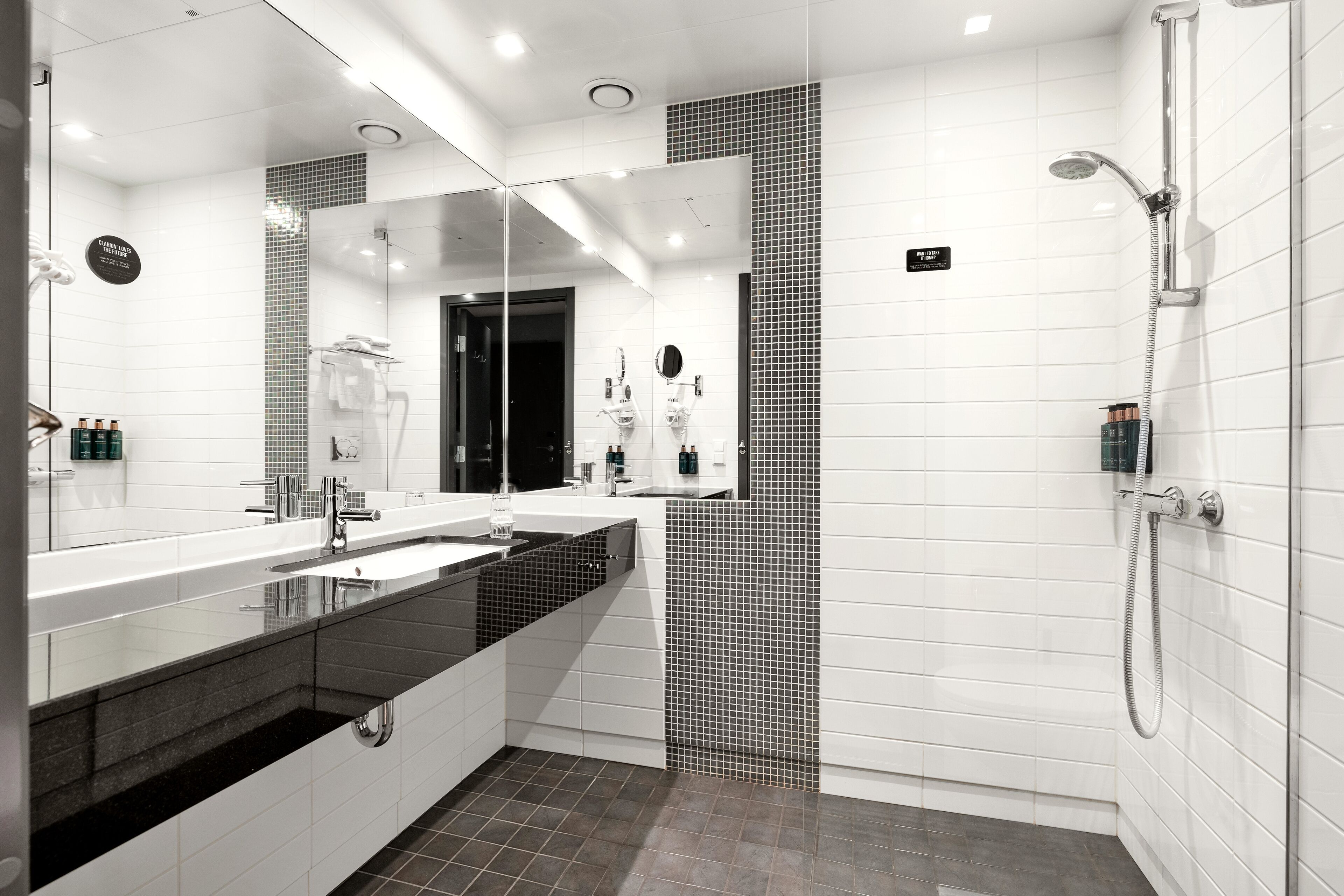 Une salle de bain moderne dotée d’un grand miroir, de deux vasques, d’une zone douche et d’un sol carrelé.