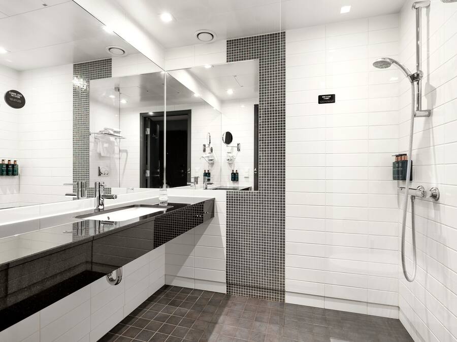 A modern bathroom with a large mirror, dual sinks, a shower area, and a tiled floor.