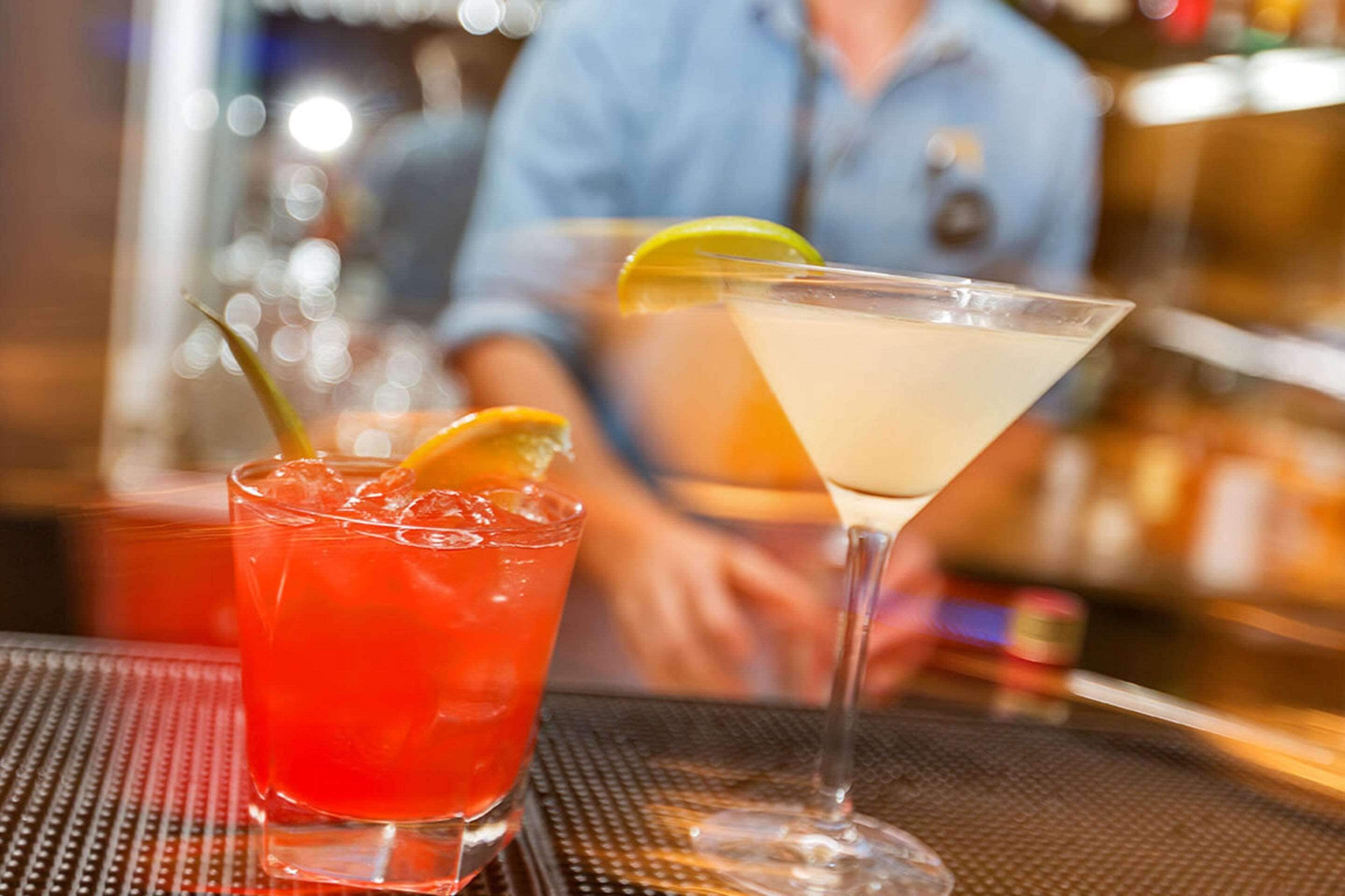 Zwei Cocktails auf einer Bar, im Hintergrund verschwommen eine Person.