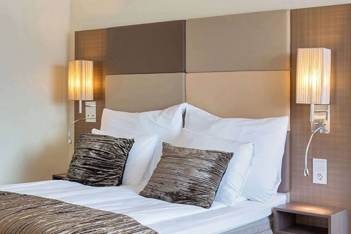 A hotel room with a large bed, two bedside lamps, and a headboard with a light panel.