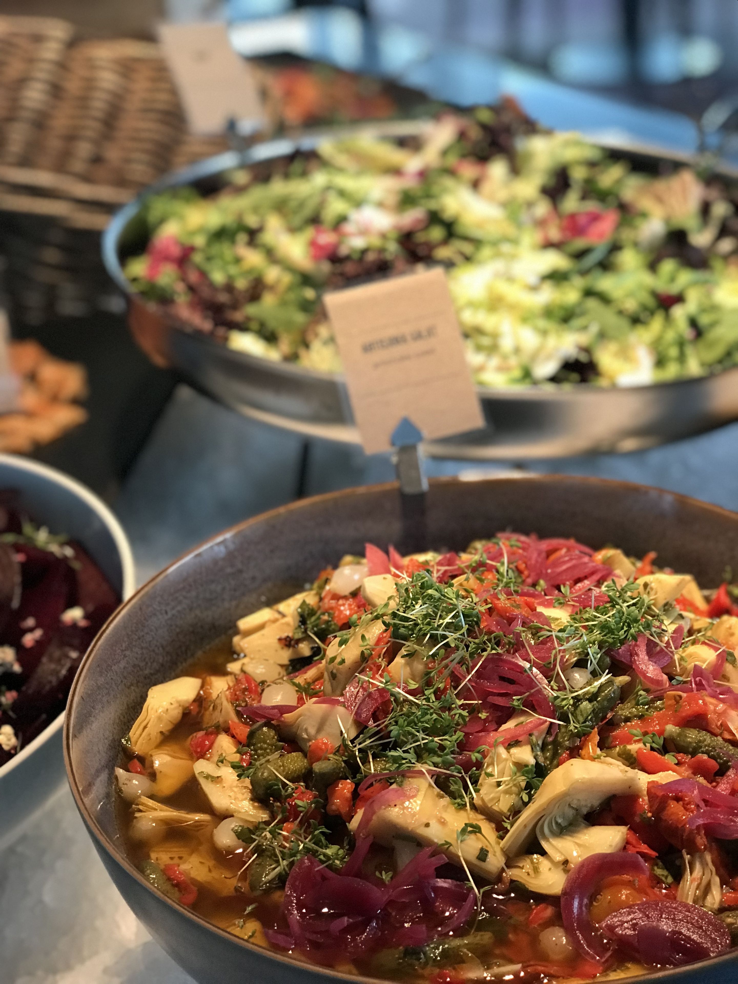 Un bufé con diversos platos, incluyendo un tazón de sopa con verduras y hierbas, y una ensalada con hojas verdes y vegetales.
