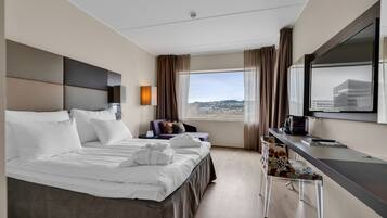 Habitación de hotel moderna con una cama grande, un escritorio y una silla. Se ve una ventana con vistas a la ciudad.
