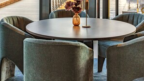Un espace repas moderne avec une table ronde et des chaises rembourrées, offrant une vue sur un paysage urbain avec des bâtiments et un front de mer.